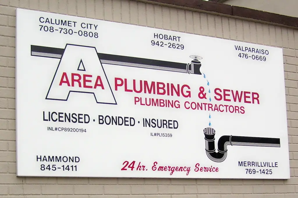 The Area Plumbing & Sewer sign on the Hammond shop wall, listing both state licence numbers and 24 hour emergency service